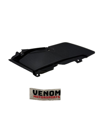 A black carbon-fiber-textured motorcycle or scooter side panel, displayed on a scratched light gray floor with a Venom Motorsports sticker below it.